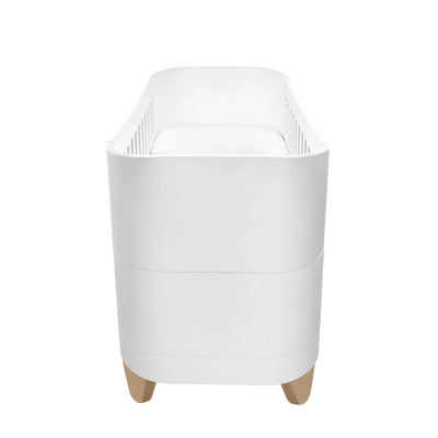 Side profile view of the white Serena cot bed with smooth curved edges, slatted interior sides, and natural wood legs on a clean white background.