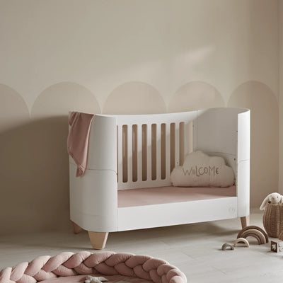 Soft blush-toned nursery featuring a white Serena toddler bed styled with pink bedding, a braided floor cushion, and neutral décor accents for a calm and cozy space.