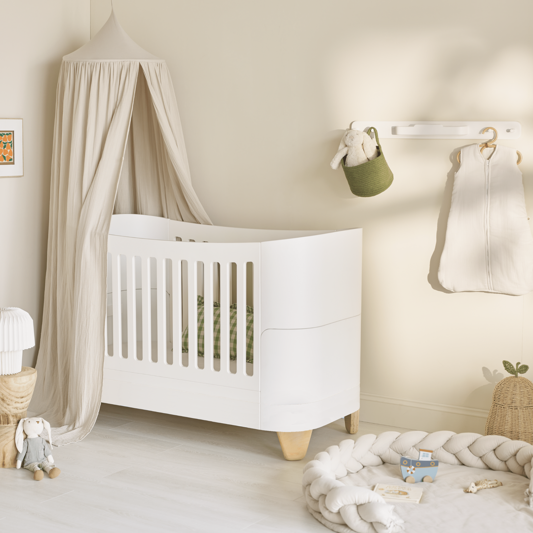 Gaia Baby Serena Cot Bed with natural legs in a nursery. Image also shows the Maia Canopy in Sand over the cot