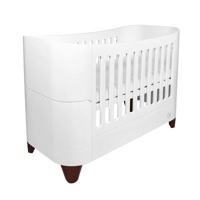 Modern white cot bed with smooth curved sides and dark walnut angled legs, shown on a white background in a minimalist Scandinavian-style product image.
