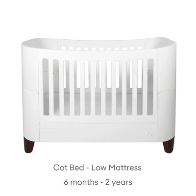 Serena cot bed with walnut legs in the low mattress position, suitable for babies and toddlers from 6 months to 2 years, displayed on a clean white background with the adjustable mattress stage clearly labelled.