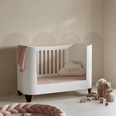Gaia Baby Serena Cot Bed in toddler bed mode with walnut legs, white wooden toddler bed with soft pink bedding in neutral nursery.