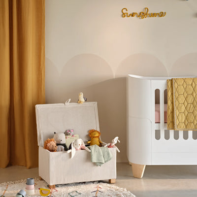 Gaia Baby Serena storage footstool in ecru corduroy used as a nursery toy box beside cot