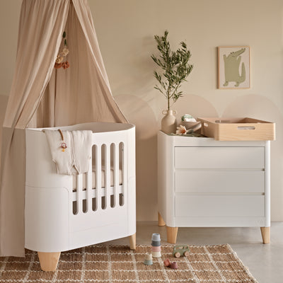 Gaia Baby Serena Mini Cot and Dresser Changer in White and Natural wood, styled in a neutral nursery with a canopy, changing station, woven rug, and soft décor accents.