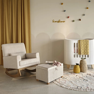 Gaia Baby Serena Mini Cot in white with rocking chair and ottoman in a modern nursery, neutral tones with soft textiles and wooden accents.