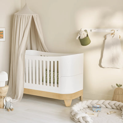 Gaia Baby Serena cot bed in white and natural wood styled in a neutral nursery with a muslin canopy, soft furnishings and natural décor.