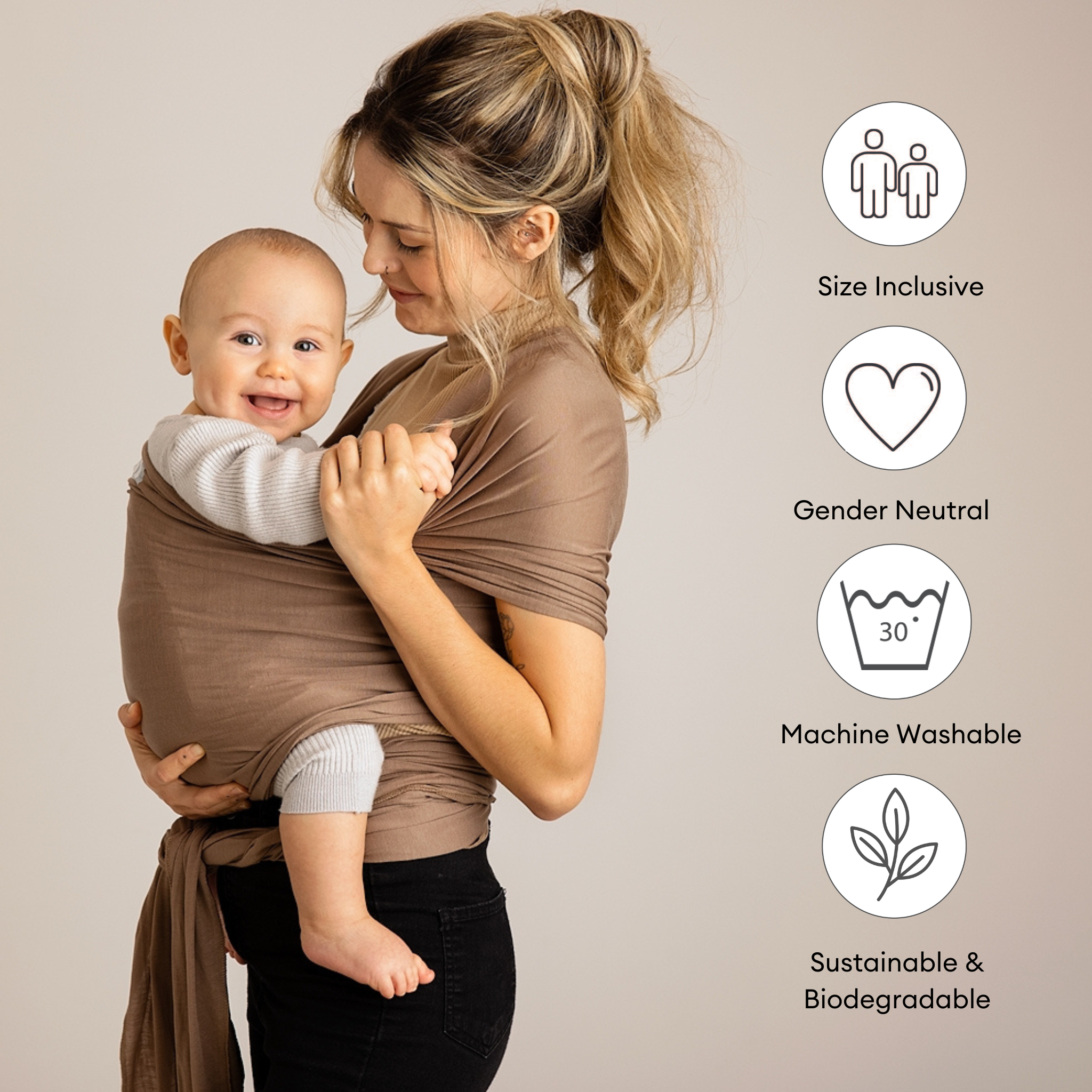 Mutter trägt ihr Baby in einem dehnbaren Gaia Baby-Wickeltuch aus muskatnussfarbener Bio-Baumwolle mit abgebildeten Auszeichnungsabzeichen.