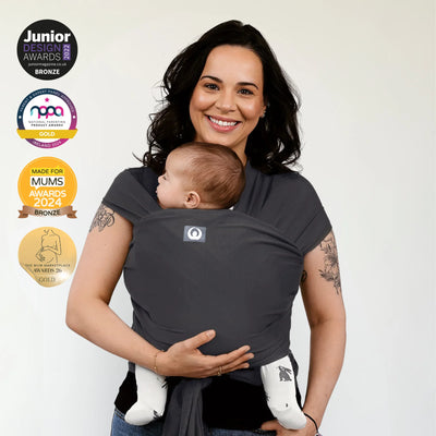 Woman wearing a graphite baby wrap holding a baby, with awards displayed on a white background.