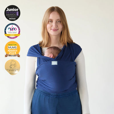 Mother carrying newborn in Gaia Baby stretchy wrap in midnight blue with award badges displayed