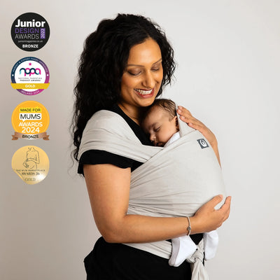 Mother carrying newborn in Gaia Baby stretchy wrap in silver grey organic cotton with award badges displayed