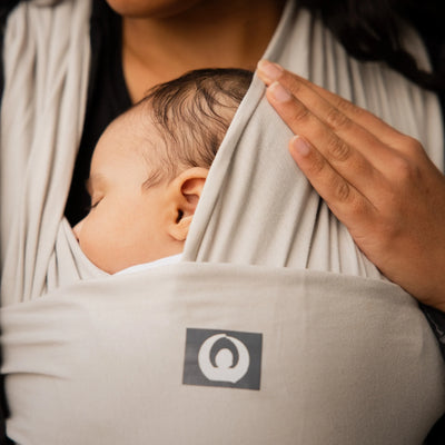 Sleeping baby in Gaia Baby silver grey stretchy wrap carrier held close to parent