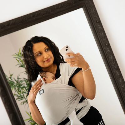 Mother taking mirror selfie while carrying baby in Gaia Baby stretchy wrap in silver grey organic cotton