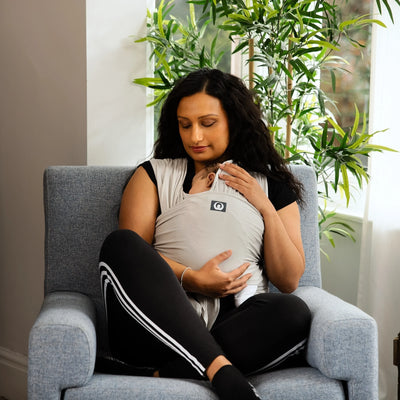 Mother sitting in chair holding newborn in Gaia Baby stretchy wrap in silver grey organic cotton at home