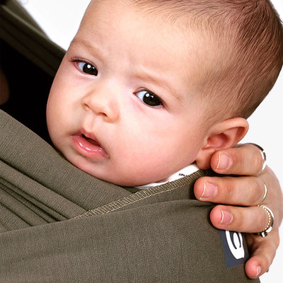 Close-up of baby resting in a forest green stretchy wrap against a parent’s chest.
