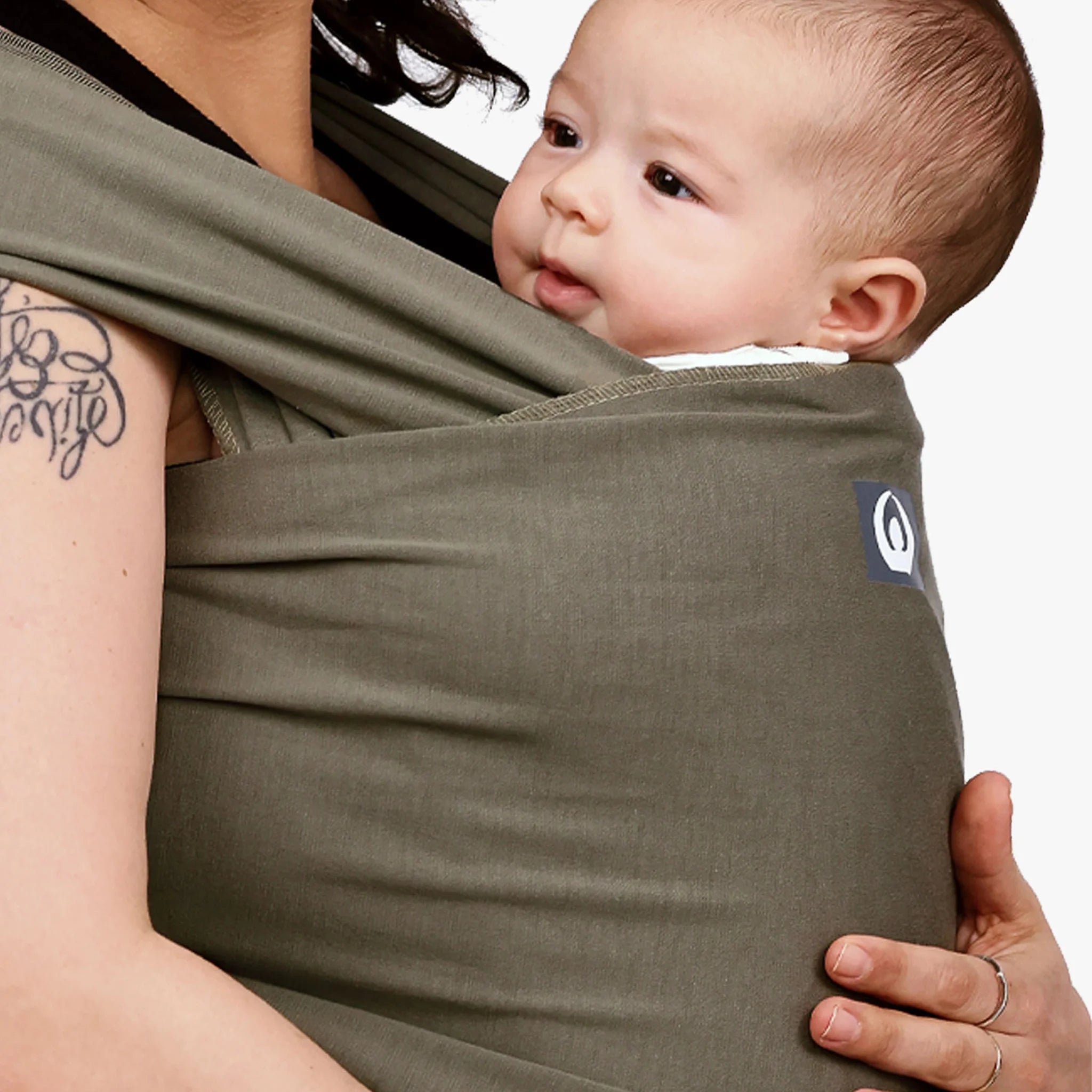 Close-up of baby in a forest green stretchy wrap being held against parent’s chest.