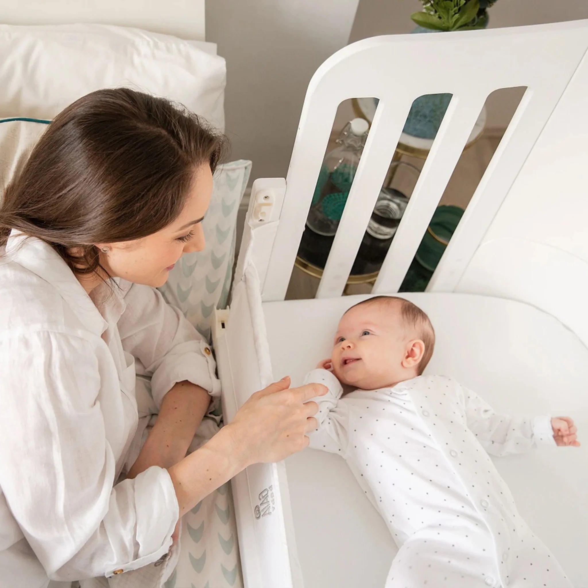 Baby lying in Gaia Baby Serena co-sleeper while mother interacts beside the bed