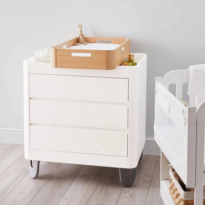 Gaia Baby Serena white nursery dresser with wooden changing tray and baby essentials next to a cot