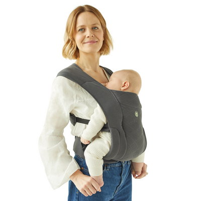 Madre rubia con la mochila portabebés Gaia Baby Newborn Plus. Su bebé duerme tranquilamente en el portabebés.