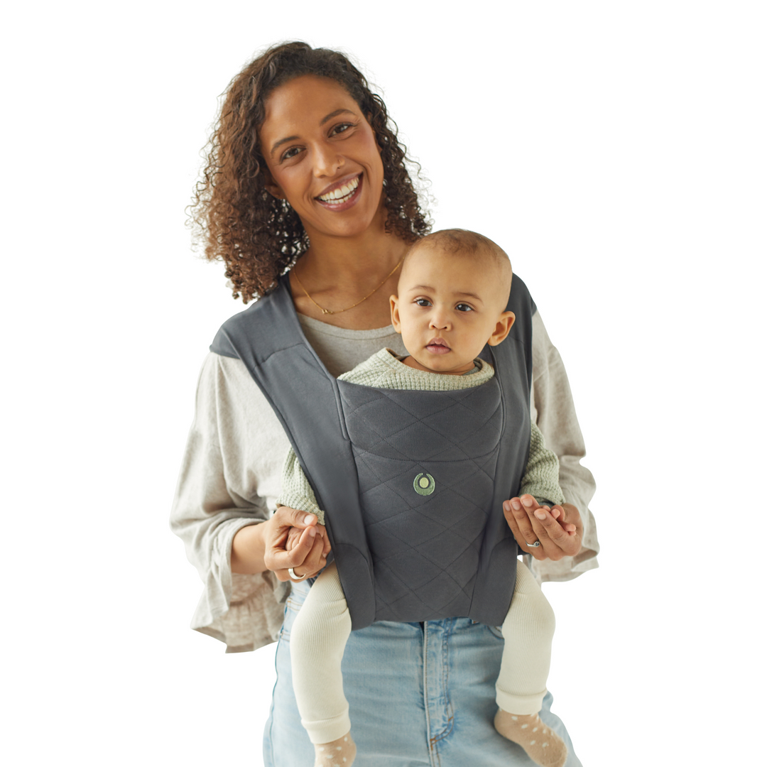 Smiling brown haired mother wearing Gaia Baby Newborn Plus Organic Cotton Carrier with baby in the world facing position facing outwards