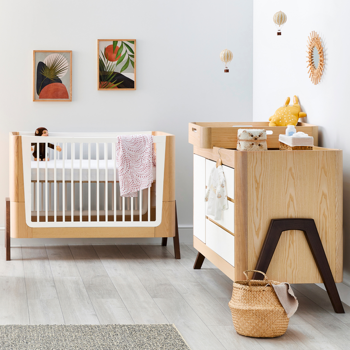 Lifestyle Image of a nursery showing Gaia Baby Hera Cot Bed, Hera Dresser and Hera Changing Station in Natural Ash and Walnut