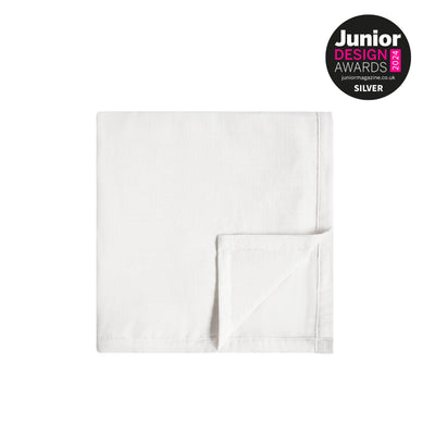 Gefaltete, weiche, weiße Musselin-Babydecke auf einem hellen, neutralen Hintergrund mit dem silbernen Abzeichen der Junior Design Awards 2024 in der Ecke.